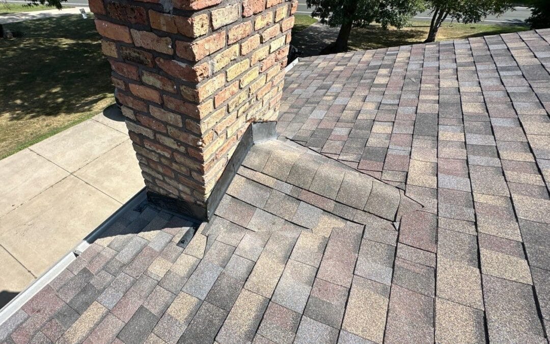 New step and counter flashing with a shingled cricket behind a brick chimney after a roof replacement