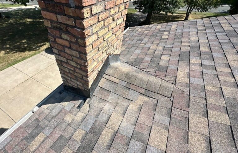 New step and counter flashing with a shingled cricket behind a brick chimney after a roof replacement