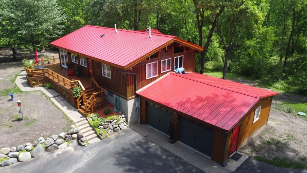 Red standing seam metal roof on a wooded Minnesota home and attached two-car garage, installed by Ascension Roofing & Siding