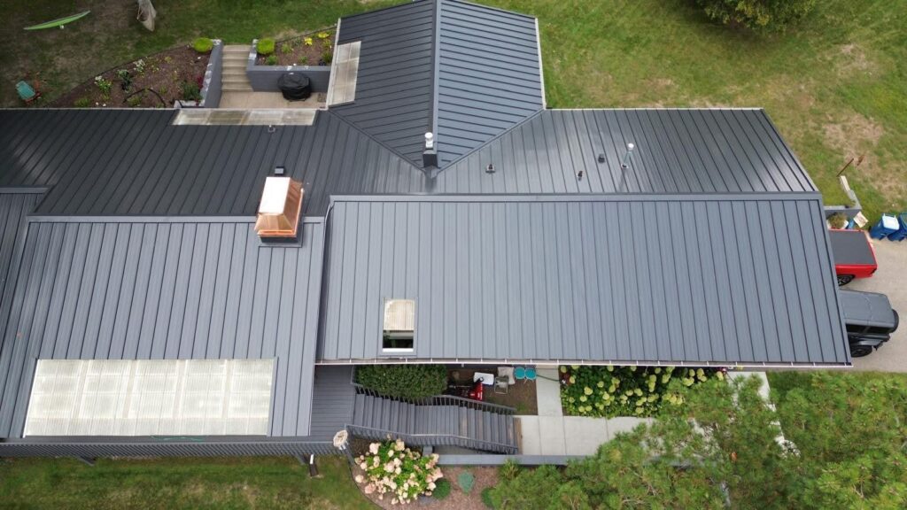 Aerial view of a large charcoal standing seam metal roof with skylights and a copper chimney cap on a Minnesota home